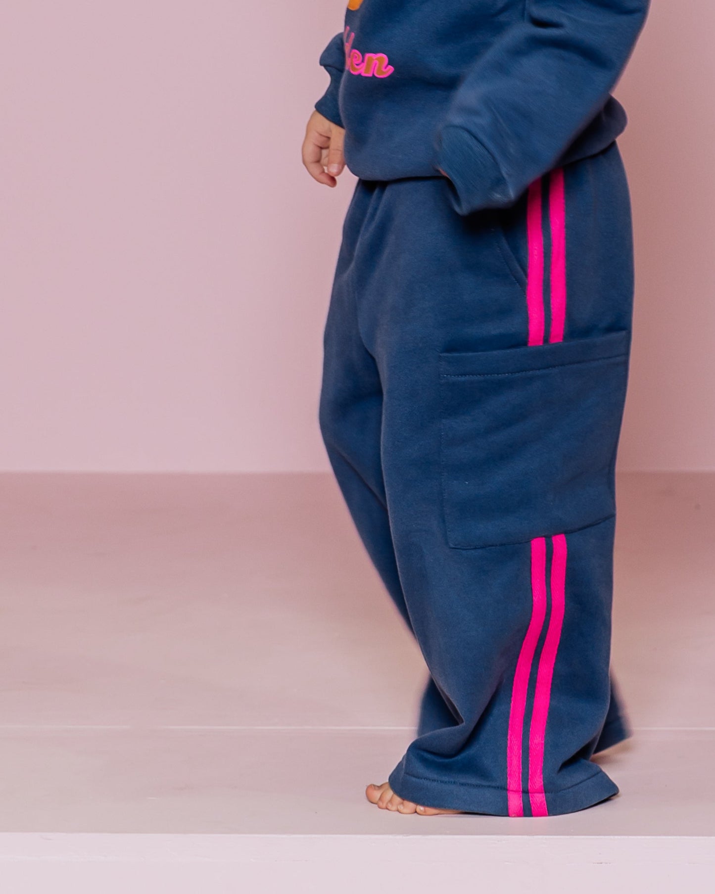 Young girl in a blue tracksuit with pink accents standing against a pink background