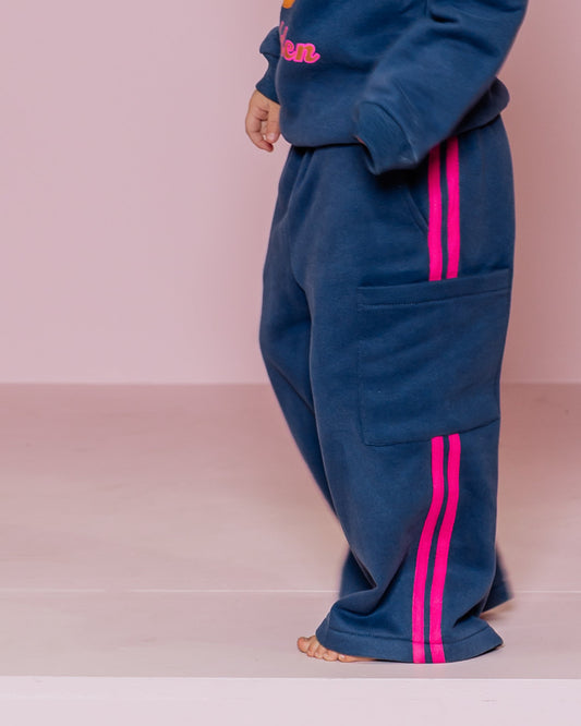 Young girl in a blue tracksuit with pink accents standing against a pink background