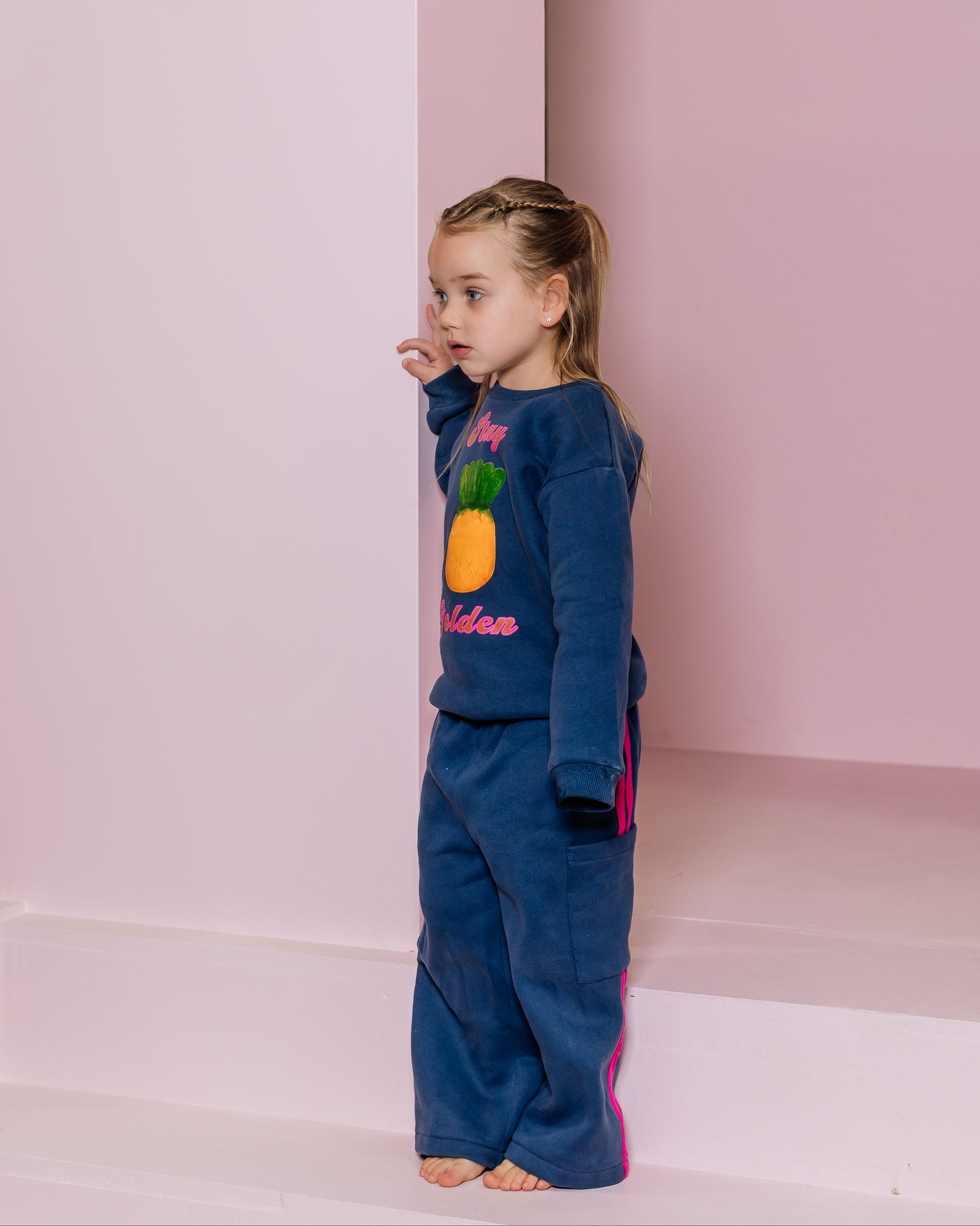 Young girl wearing a blue tracksuit with colorful designs against a pink background