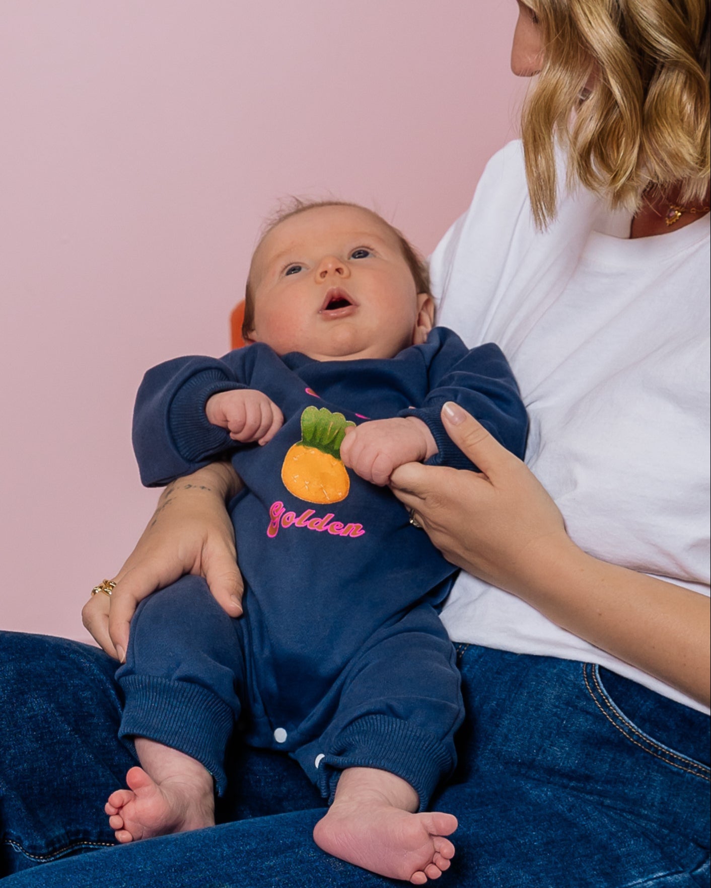 Woman sitting on a pink surface holding a baby dressed in blue.