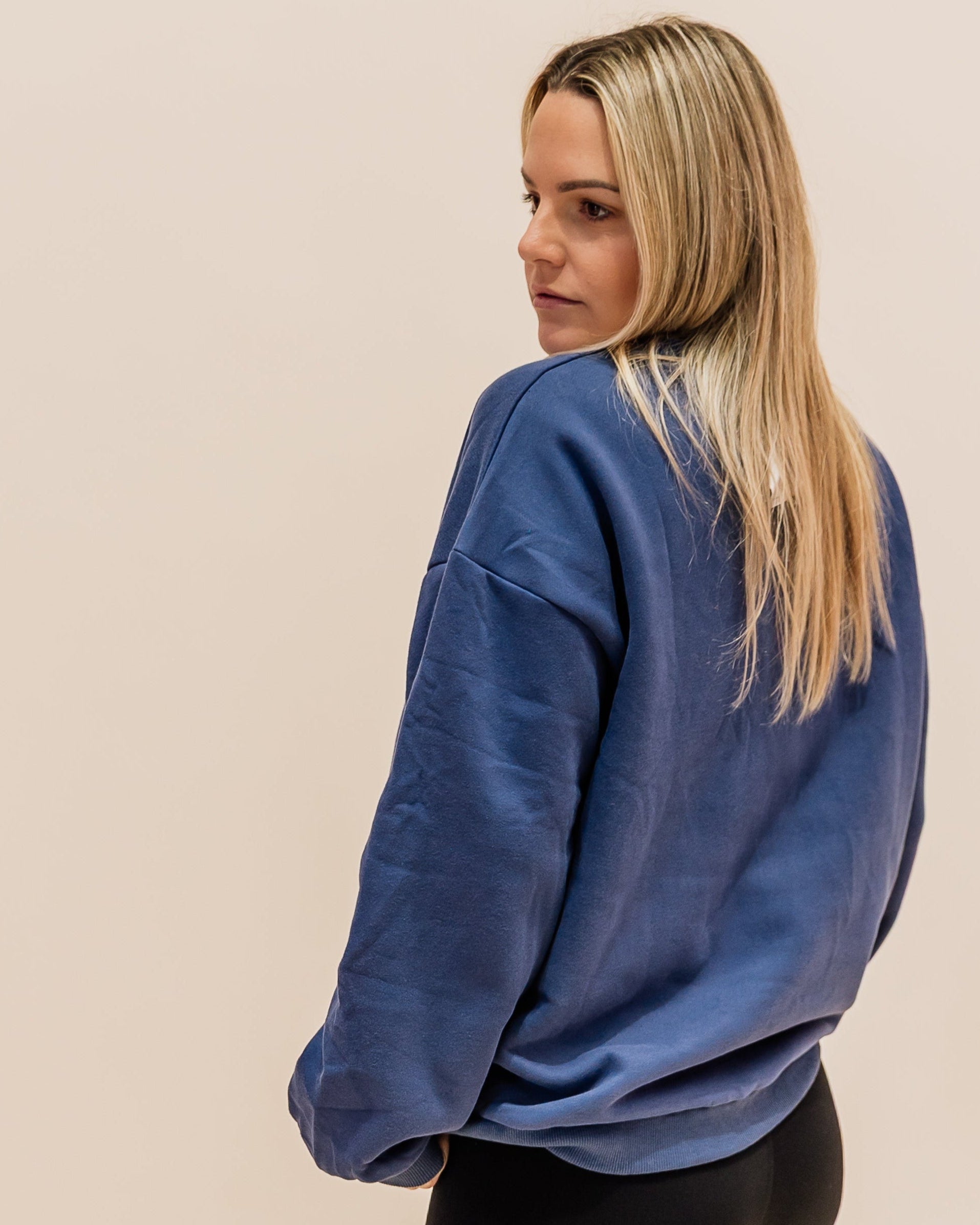 Woman wearing a blue sweatshirt, black leggings, and white sneakers with green accents on a beige background