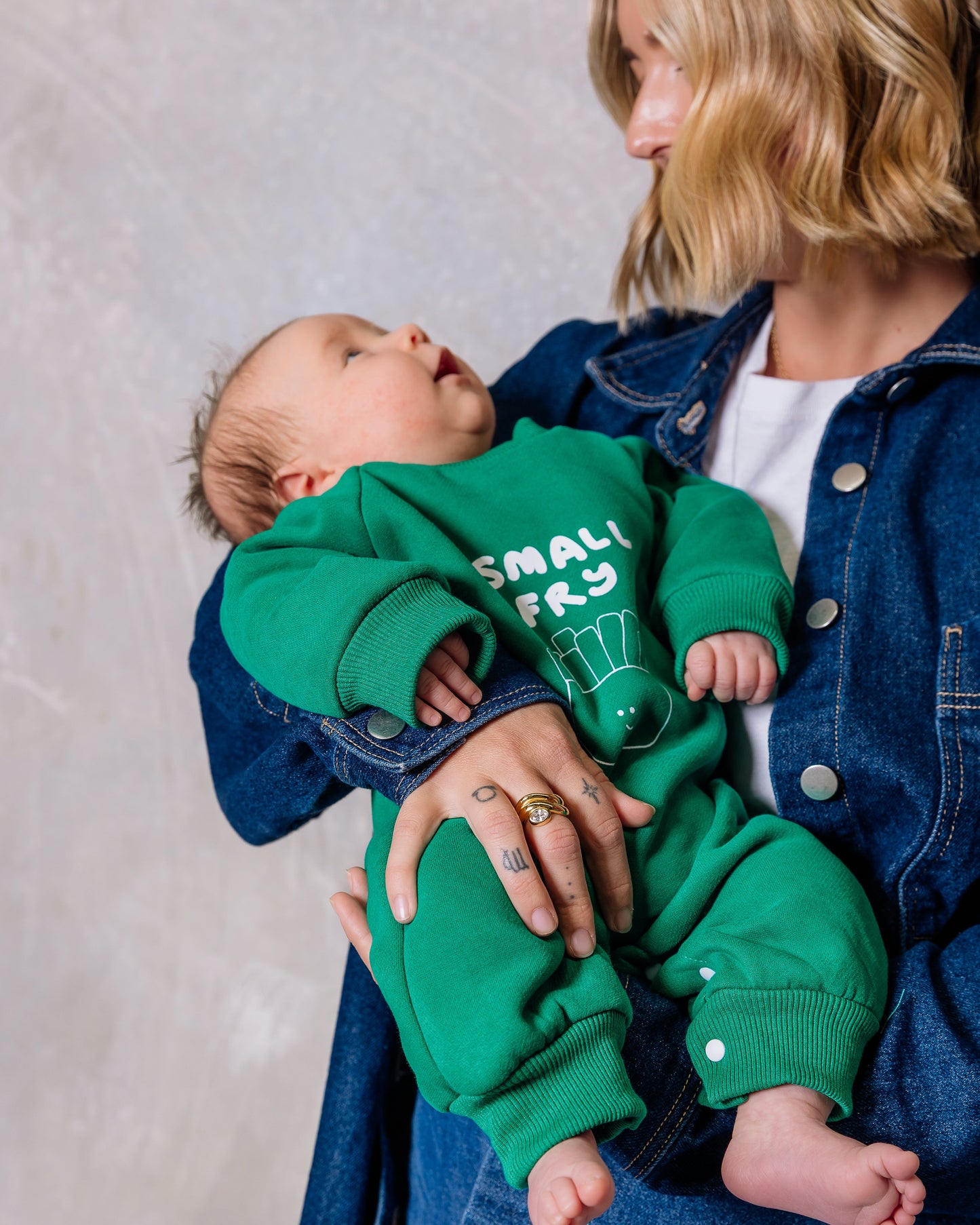 Woman holding a baby wearing a green 'Small Fry' outfit against a plain background