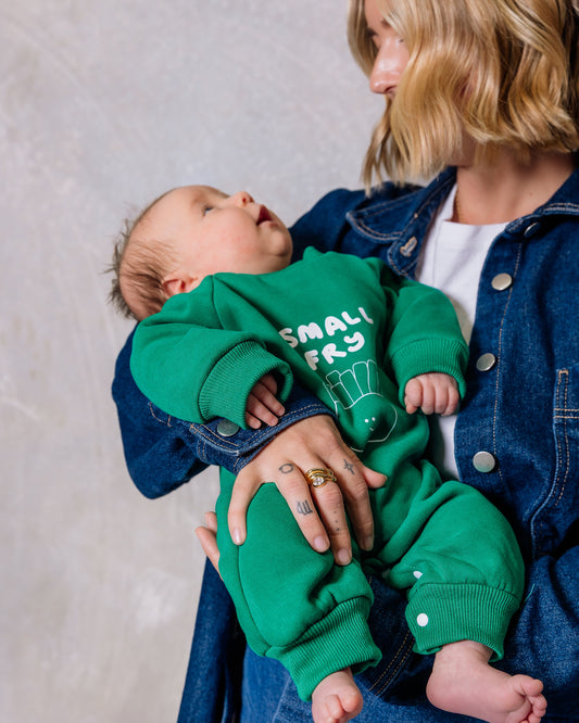 Woman holding a baby wearing a green 'Small Fry' outfit against a plain background