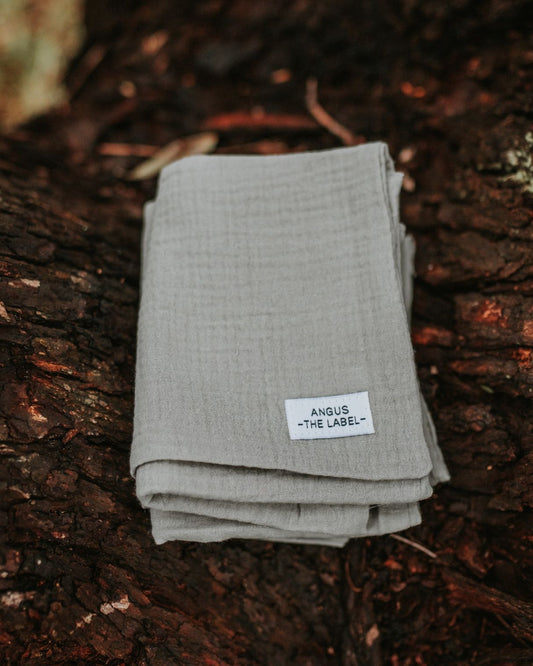 Three warm slate brown burp cloths sit stacked on top of eachother on a tree branch