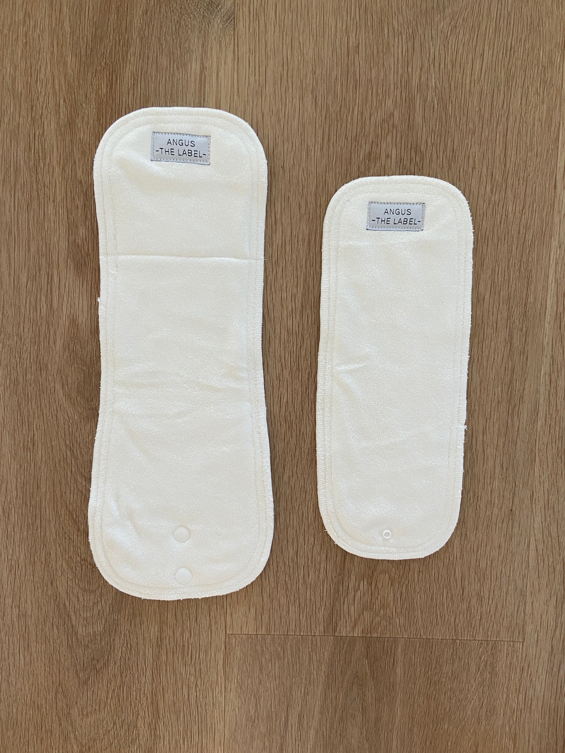 Two bamboo modern cloth nappy inserts lay flat on a wooden background