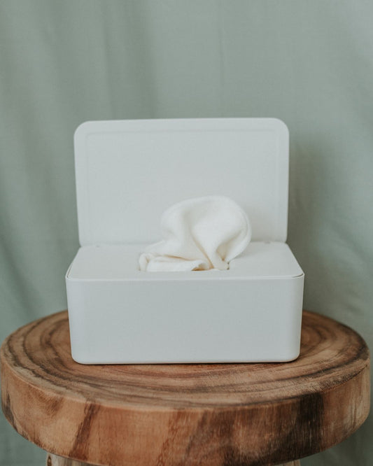 A cream plastic container sits open on a wooden side table with cream bamboo washers in it.