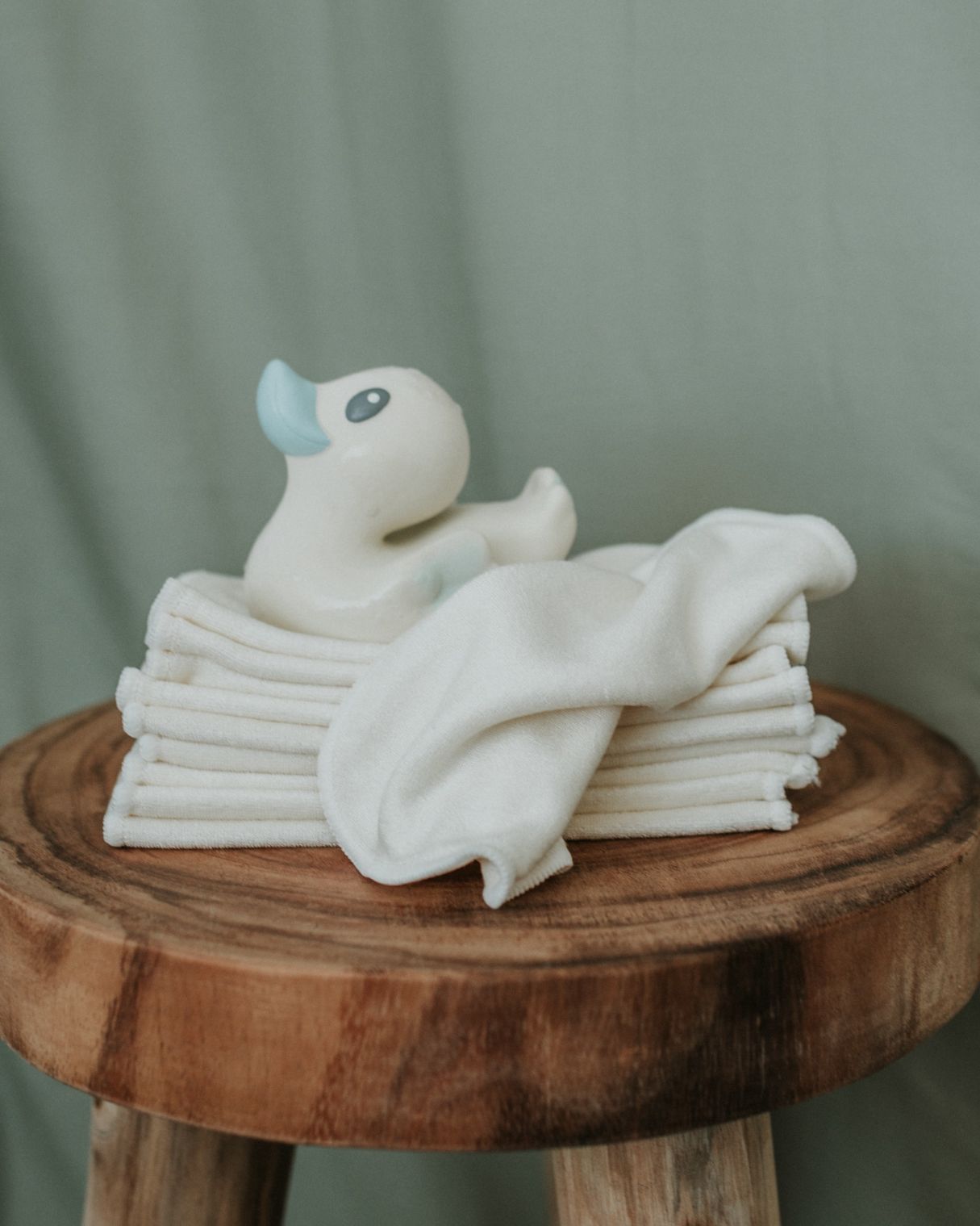 folded stack of bamboo wash cloths sitting on a wooden side table with a rubber duck on top.